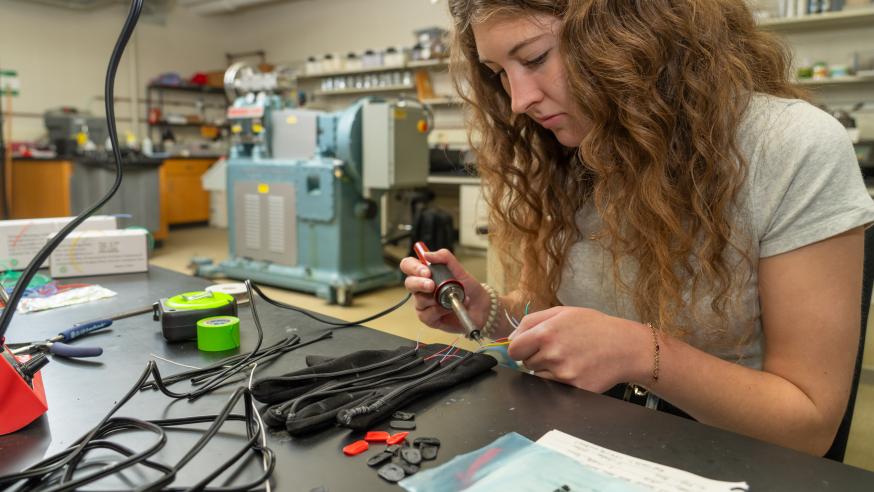 student in lab working on wiring of glove with electronics 