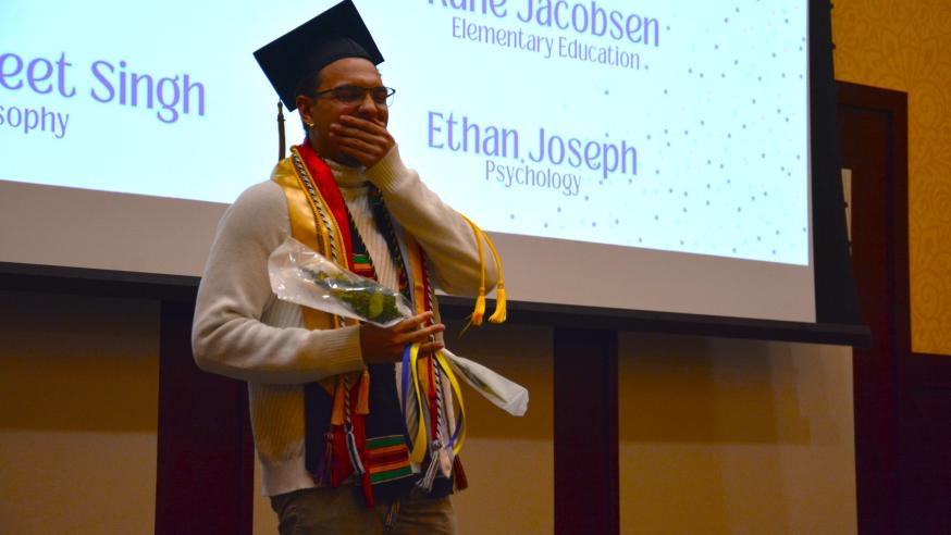 A student in a grad cap holds a bouquet while smiling
