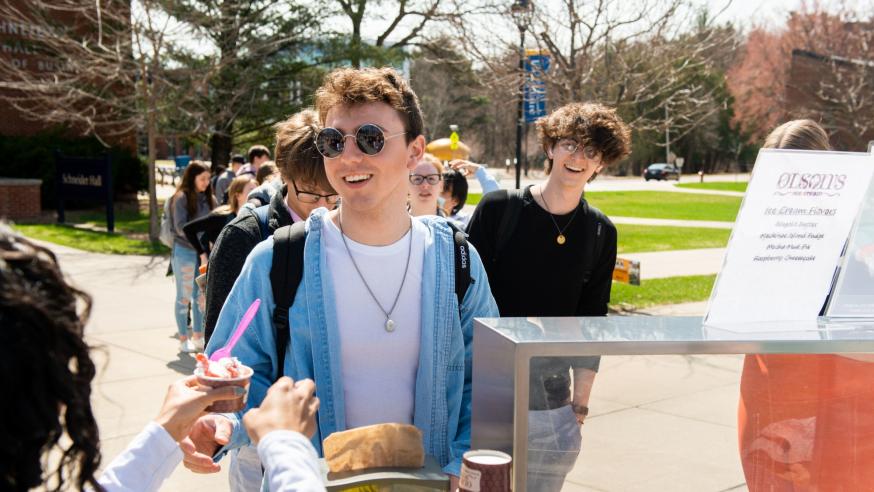Student smiles while reaching for an ice cream cone from Olson's Ice Cream.