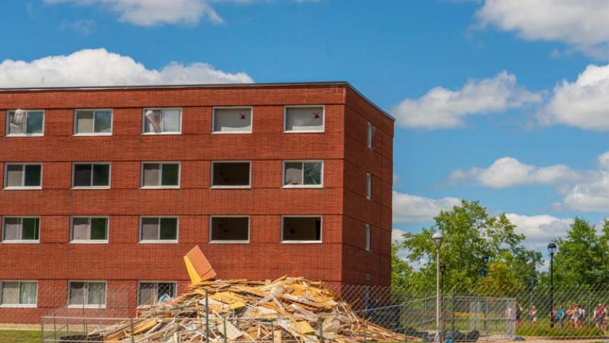 A windowless brick dorm building has a pile of rubble in front of it from a demolition project