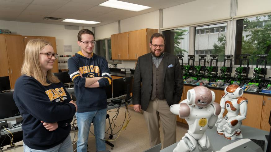 Robotics students look at their robotics equipment with a professor