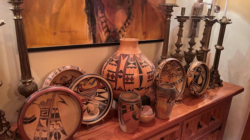 An ornate selection of southwestern indigenous pottery, displayed one a wooden hallway table, with artwork behind and tall candlesticks flanking either side