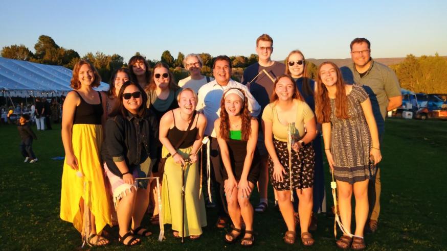 New Mexico immersion students and faculty stand in two rows, at sunset, against a New Mexico vista, smiling and dressed for a wedding