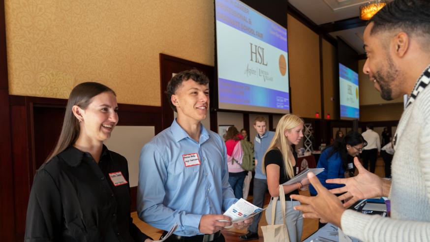 Two students attending a career fair speak with an employer at a booth