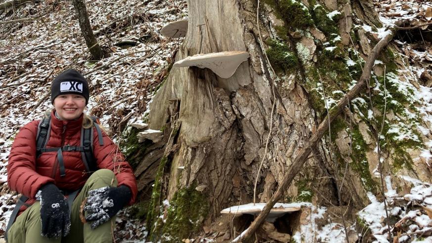 UWEC student Elva Crist sitting in hiking gear next to a tree in Iceland
