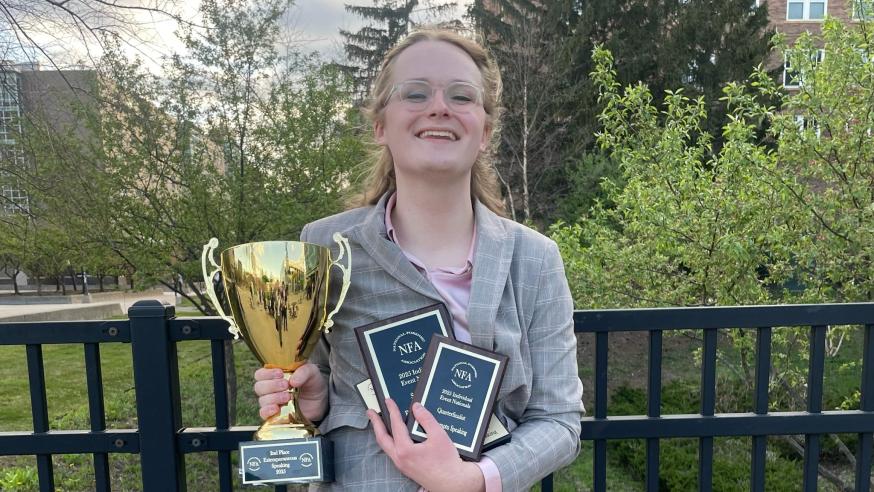 Austyn Clemen smiling and holding an embarrassment of Forensics competition riches