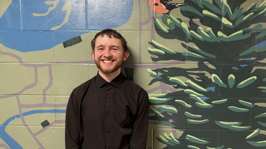 Jayson Coleman smiling in front of a mural in the Haas Fine Arts Building