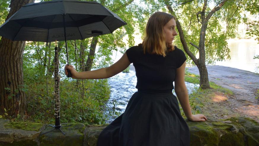 Carrie Schwartz in a black dress in the forest holds an umbrella over an oboe 