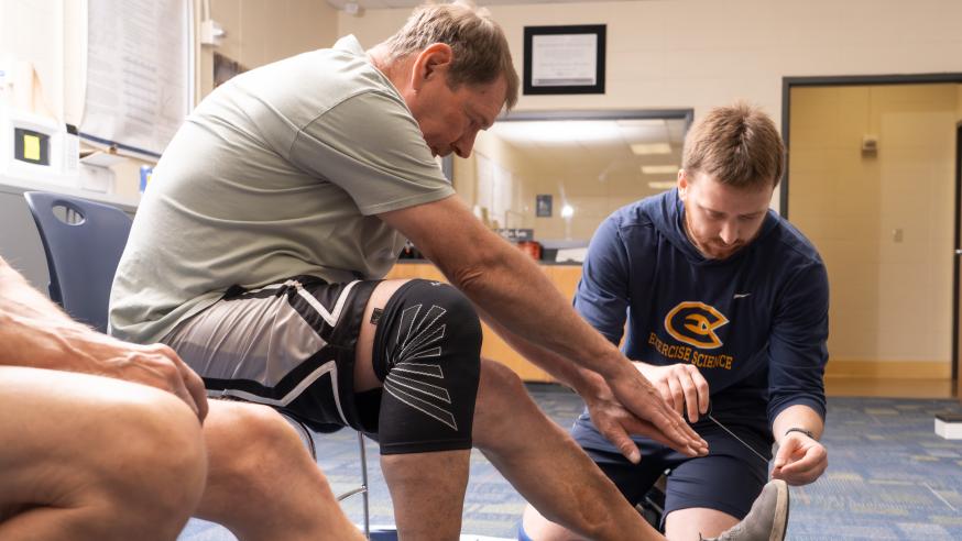 A student helps stretch a patient's leg.