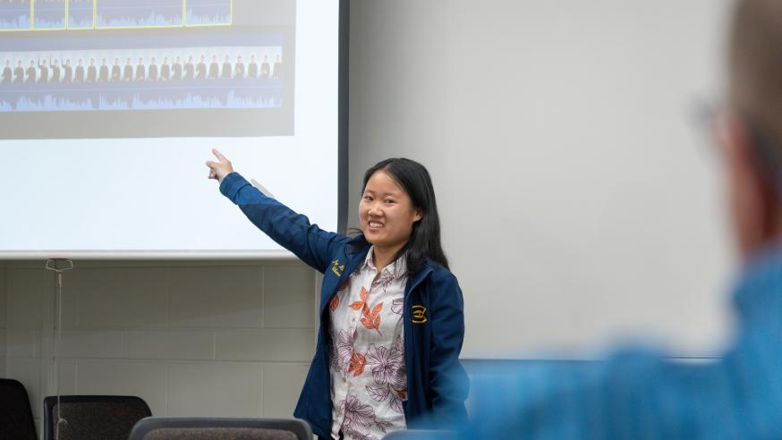 An Integrated Studies student points to a screen while presenting to a classroom. 