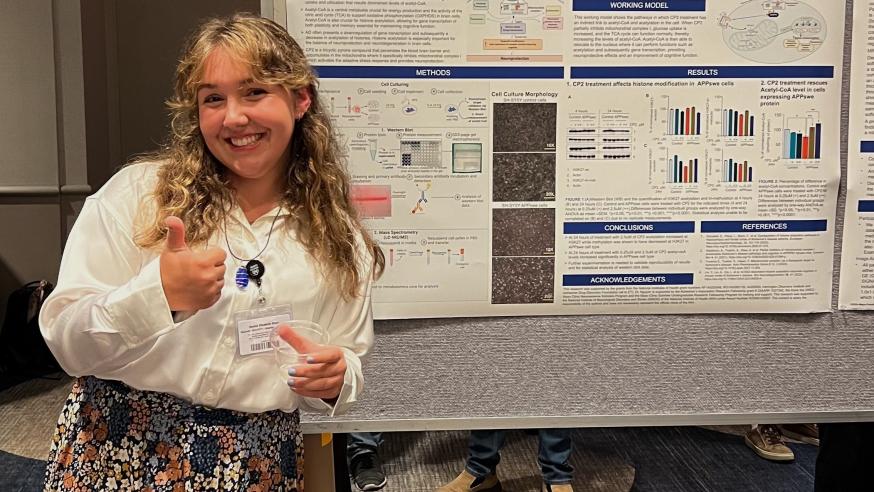 Rachel Stein smiles with a thumbs up in front of her research poster