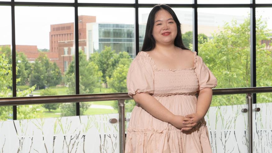 Female Asian student inside Davies Student center, pink dress, smiling.