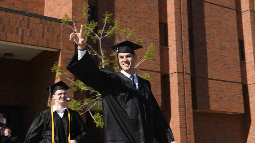 male student in graduate gown giving a peace sign