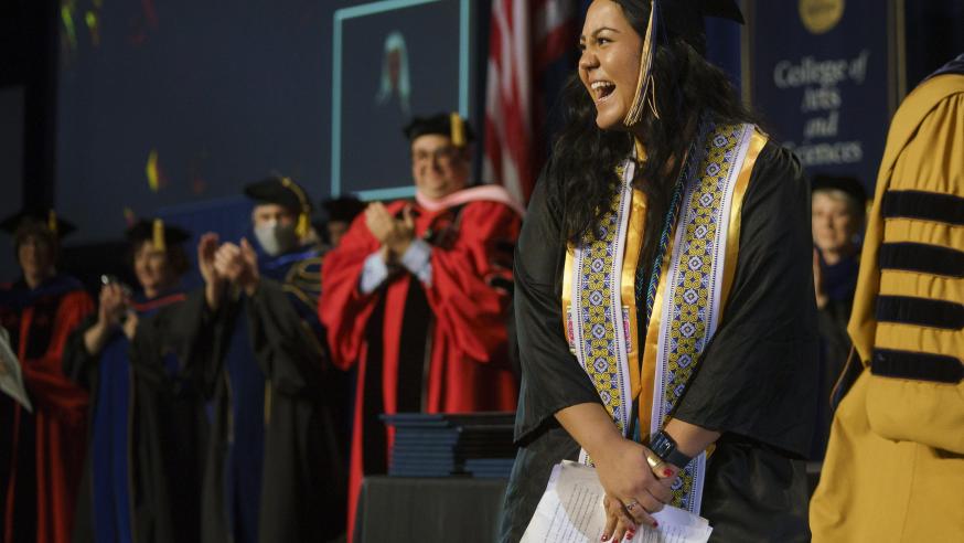female student on commencement stage smiling at the crowd