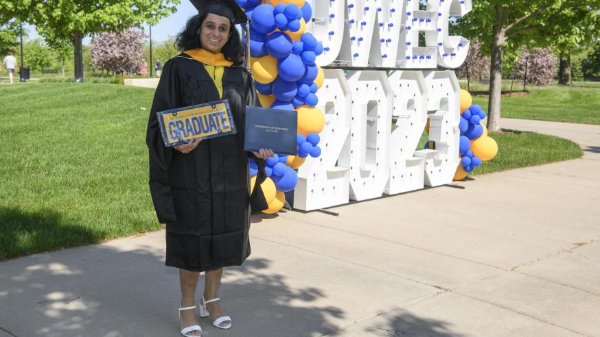 masters student in front of the lighted sign for commencement