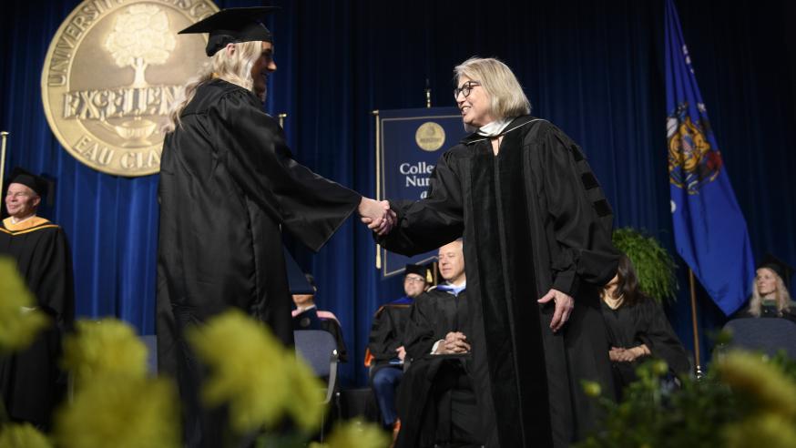 two women on stage at commencement shaking hands