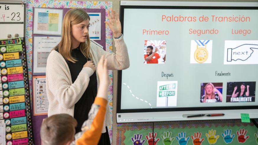 female student teacher raising her hand in front of a classroom