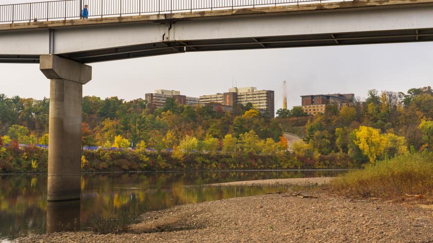 View of campus hill from the shore of the river under the footbridge