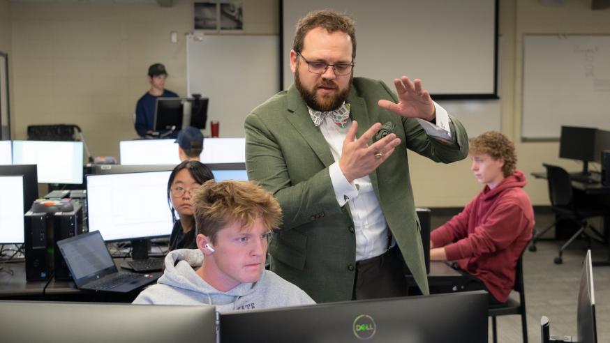faculty member in suit coat and tie among seated students in a computer science class