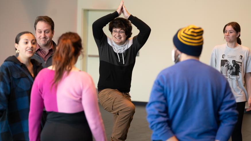 Theatre students doing some physical acting activity, one with hands above head and standing on one foot.