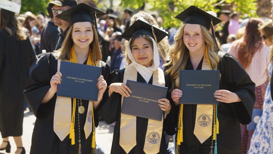 three women graduating at UWEC, in caps and gowns
