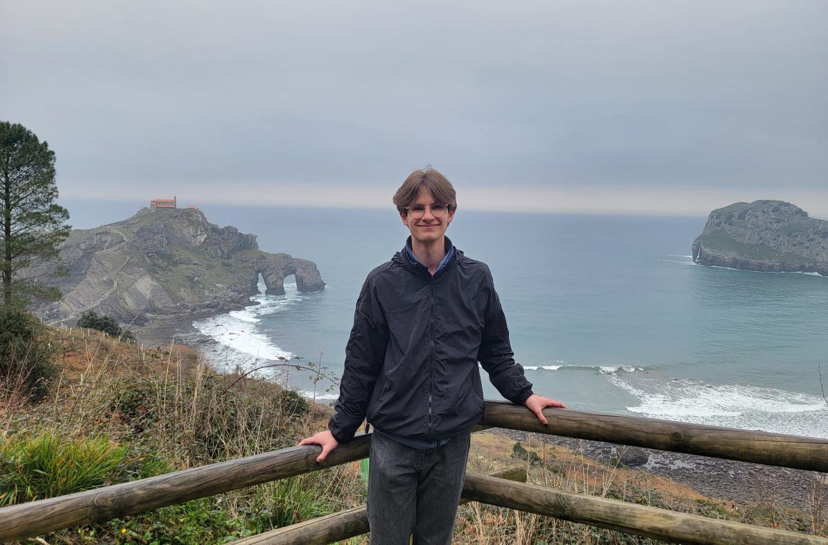 Calvin Lutzke stands in front of a railing overlooking a sea.
