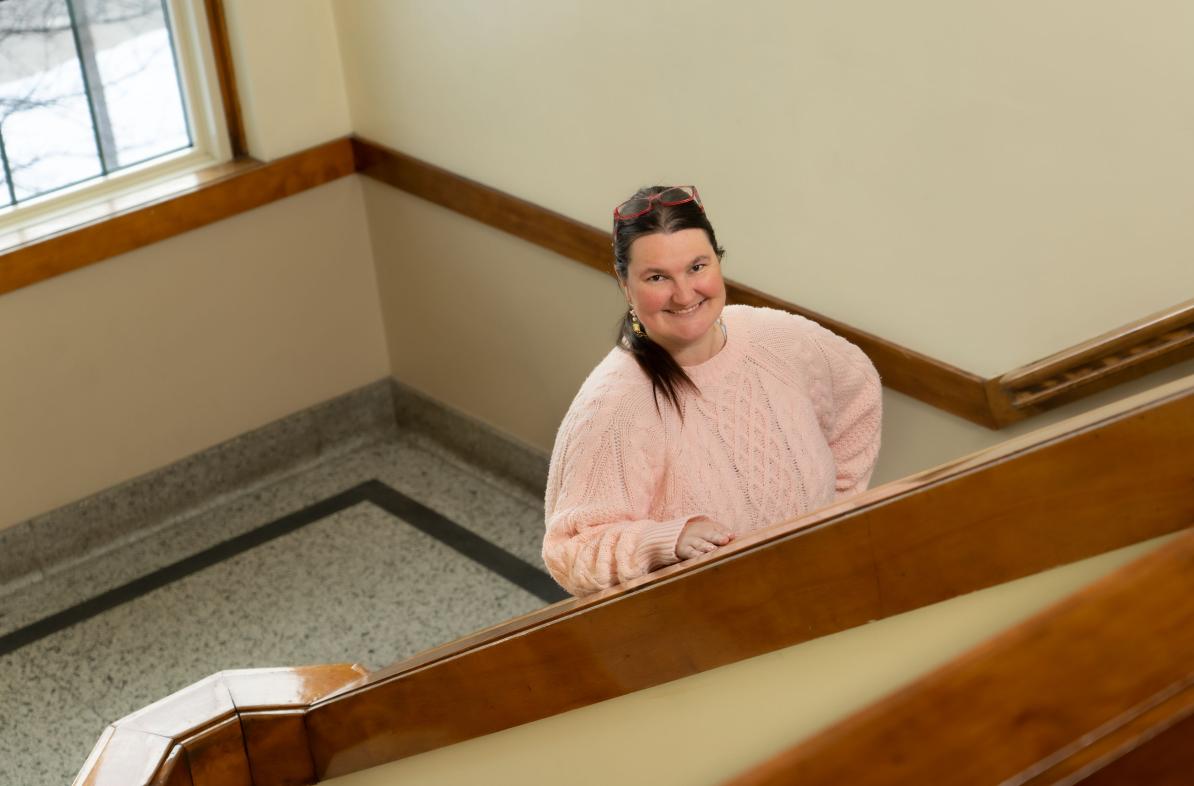 Woman with brown hair and pink sweater standing in staircase in Schofield Hall