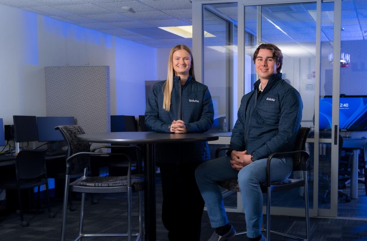 Two young alumni staff members of Solutia Consulting in branded coats 