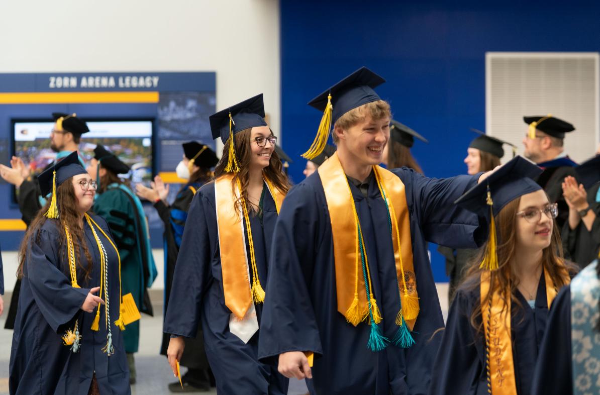 Graduates wearing graduation caps and gowns walk in a line into the ceremony on commencement day