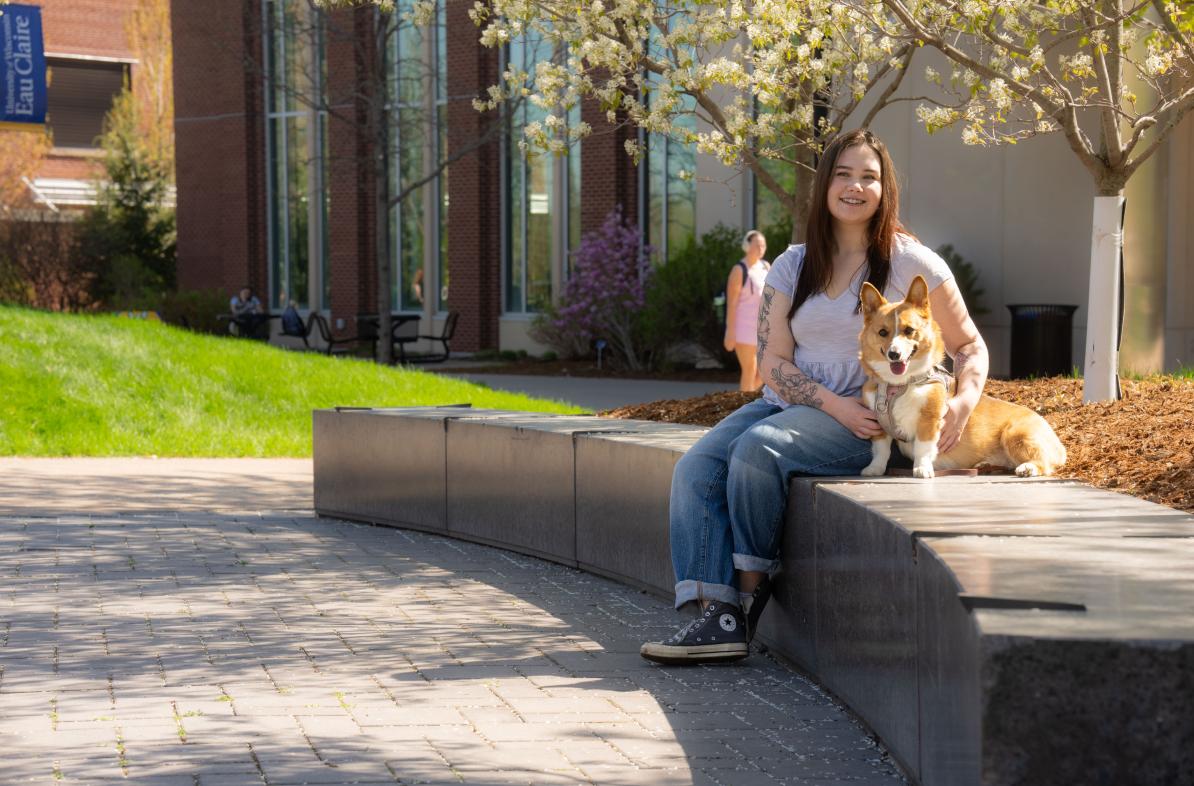 student and service dog seated on campus mall area on a sunny spring day 