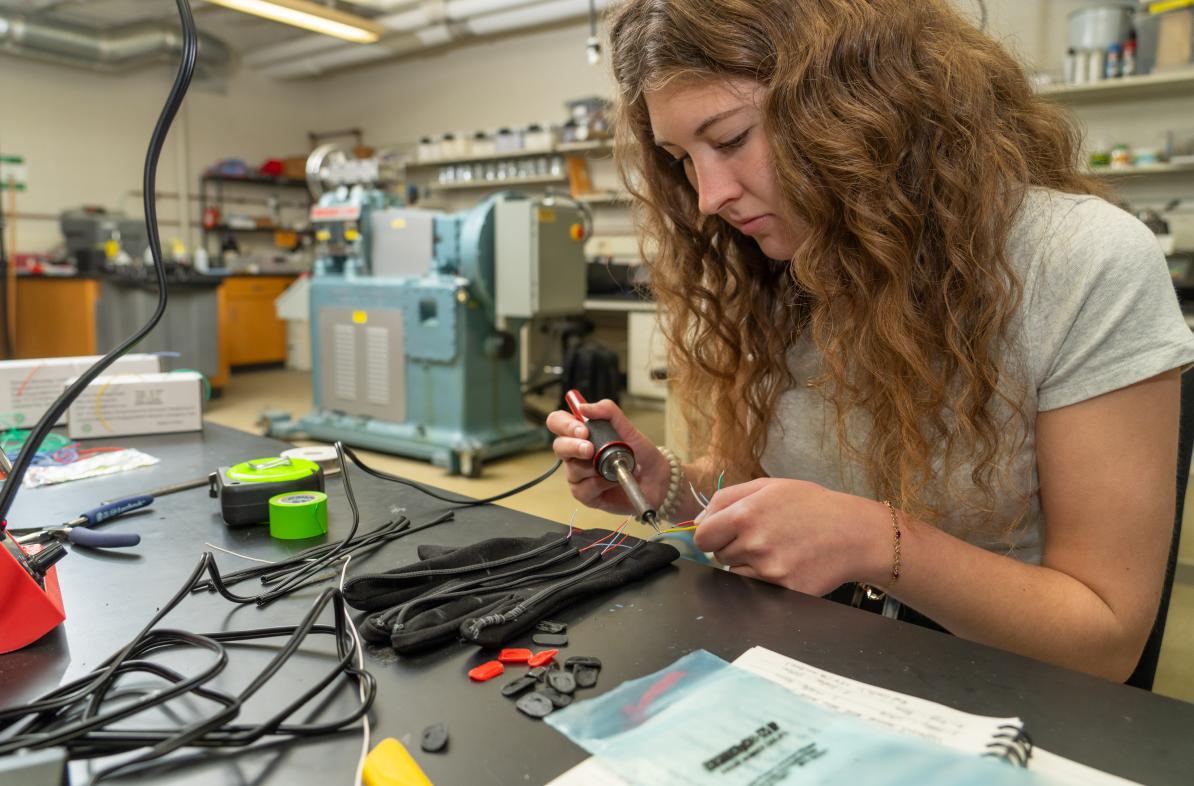 student in lab working on wiring of glove with electronics 