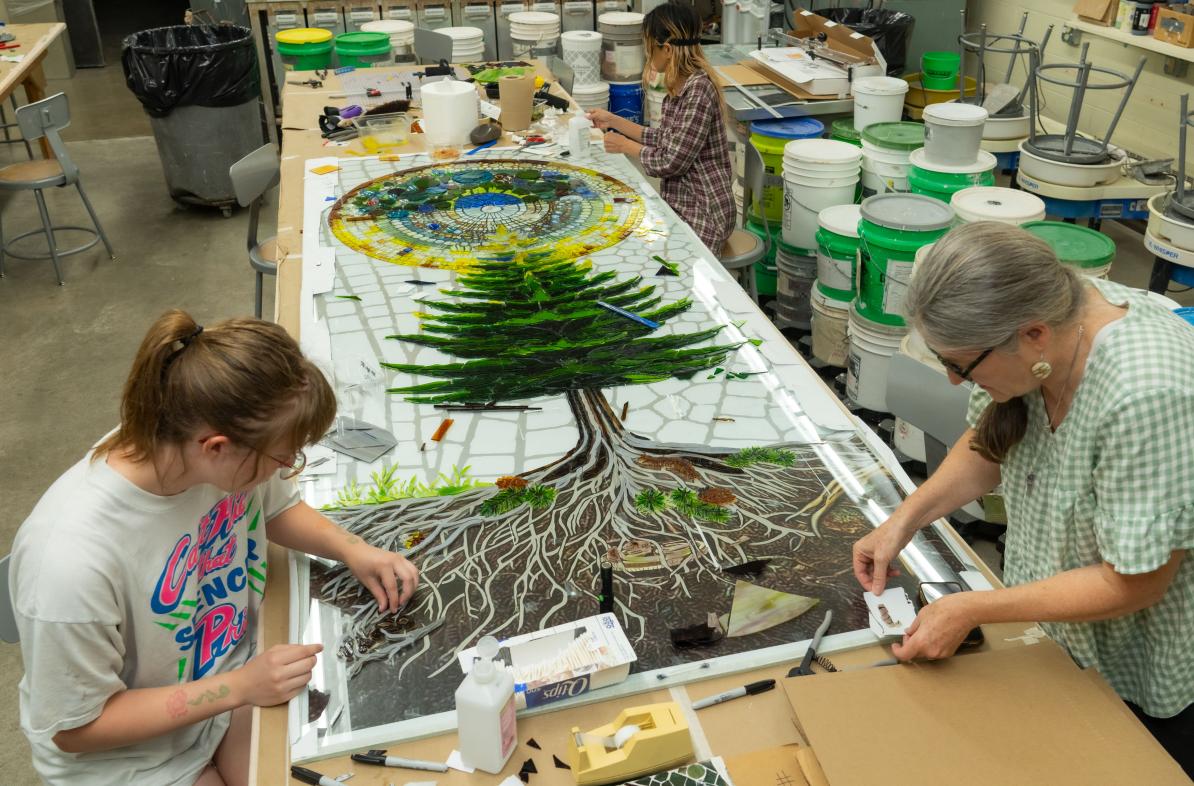 Art student and faculty making stained glass on a long table 