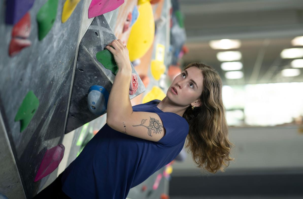 A student climbs a climbing wall looking determined.