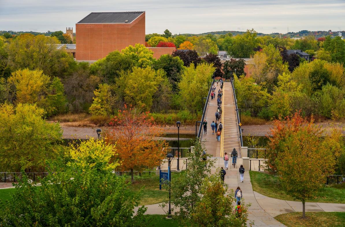 Students cross the bridge while fall colors surround them.