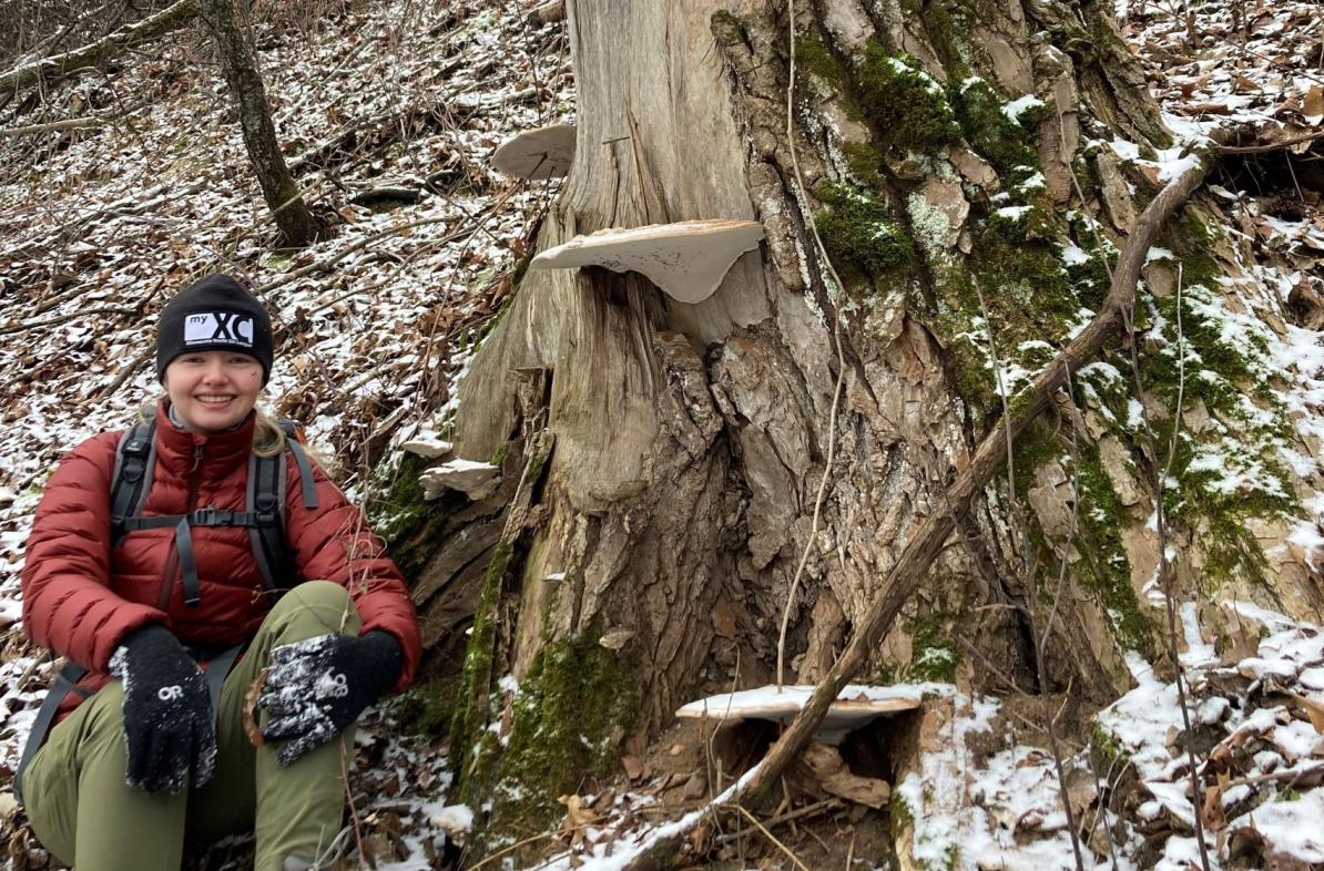 UWEC student Elva Crist sitting in hiking gear next to a tree in Iceland