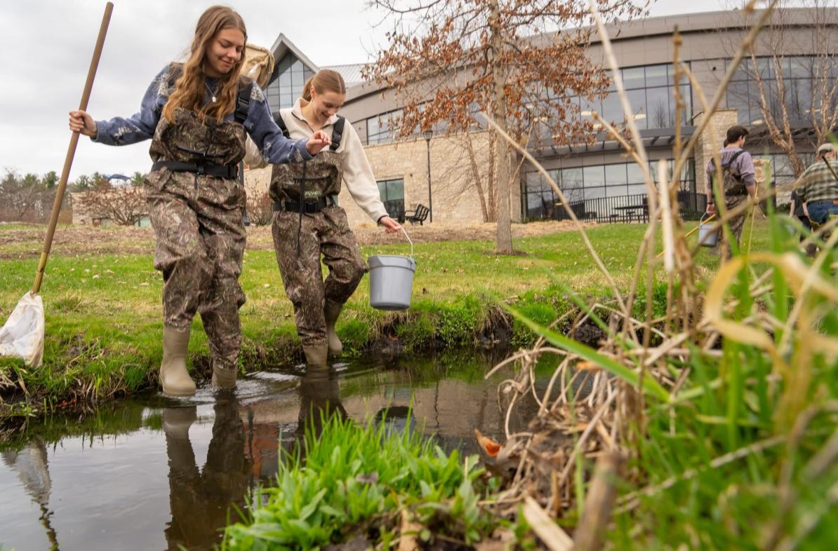 Honors students Hannah Schindler and Lexi Siegmund in camouflage waders