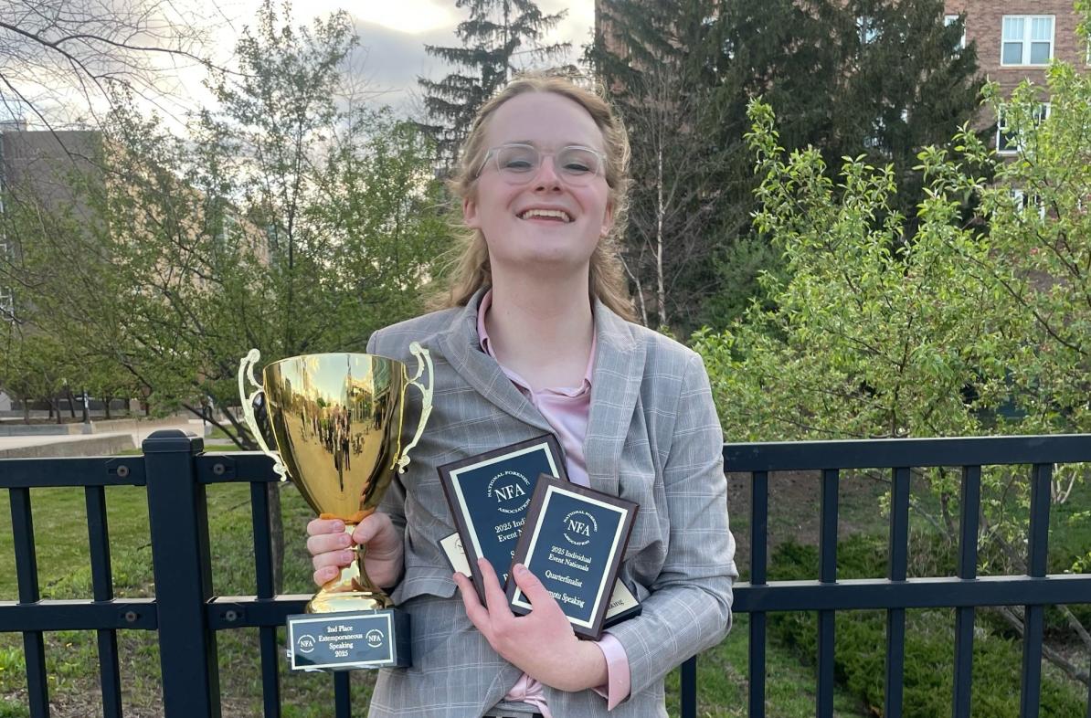 Austyn Clemen smiling and holding an embarrassment of Forensics competition riches