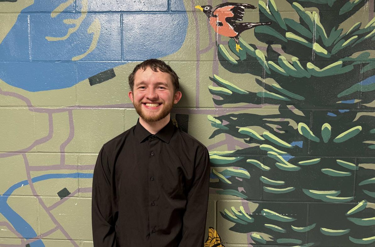 Jayson Coleman smiling in front of a mural in the Haas Fine Arts Building