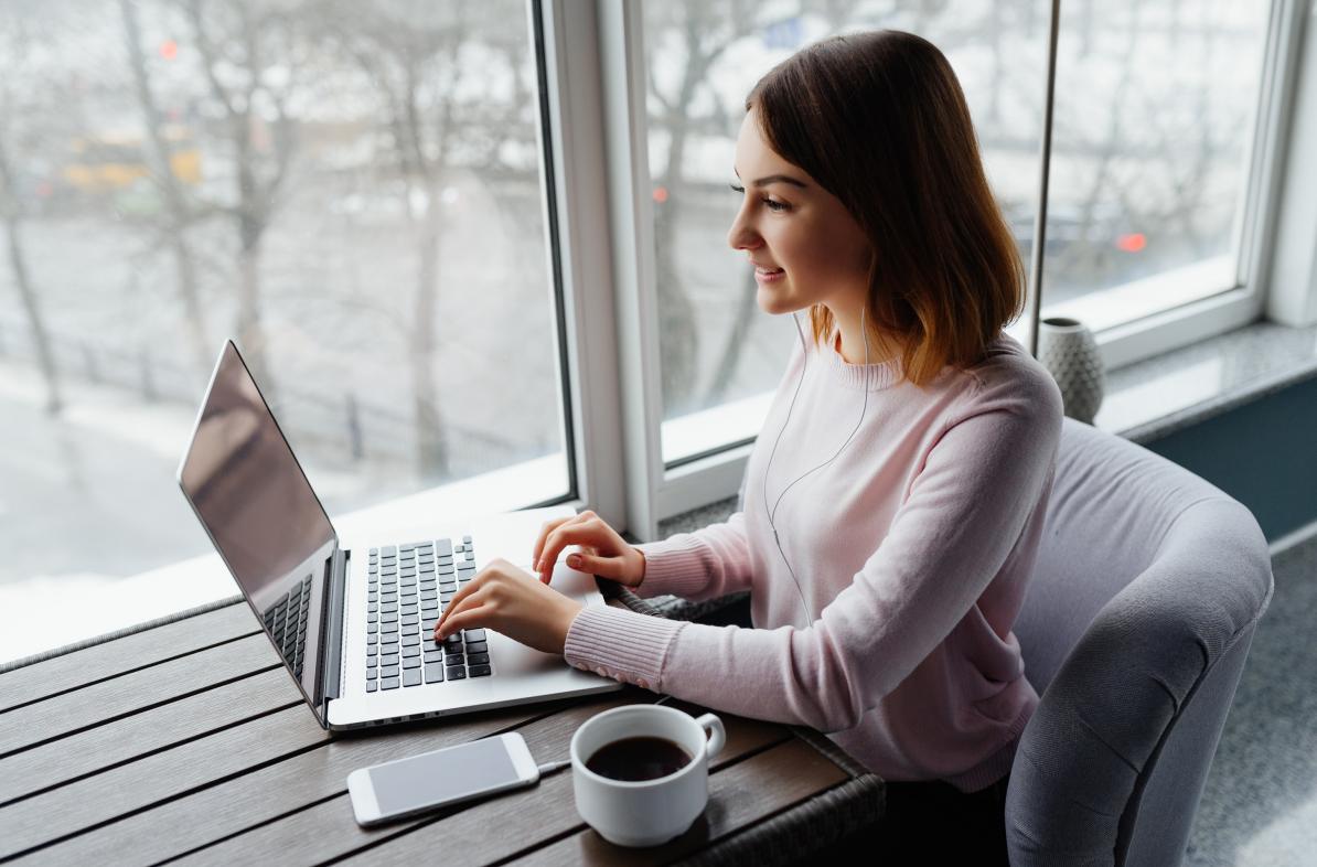 A women works on her laptop near a window.