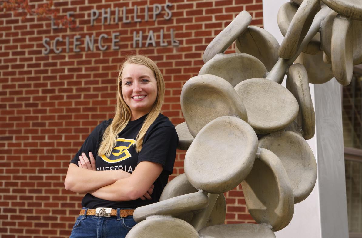 Female student leaning on sculpture outside science building