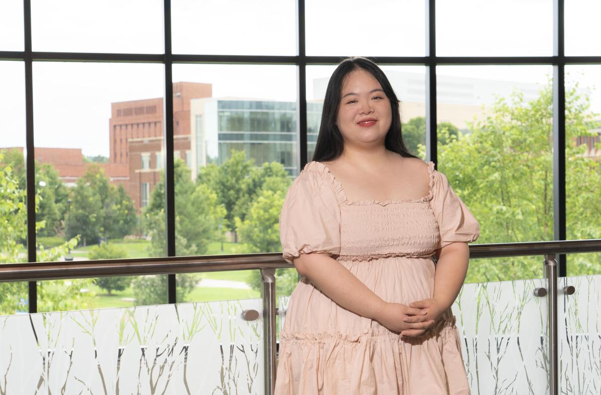 Female Asian student inside Davies Student center, pink dress, smiling.
