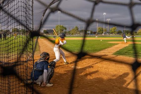 A view from behind the net showing a baseball batter preparing to hit a pitch during a game