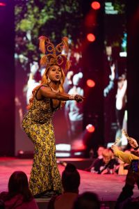 A drag performer gestures to the audience while on stage.