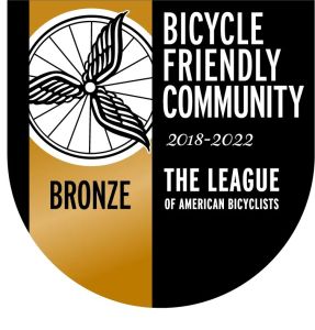 A circular logo, black and bronze, showing Bicycle Friendly Community award.