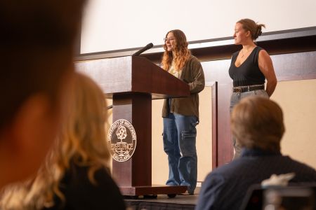 Two students speak at a podium to a crowd.