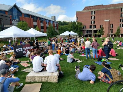 The campus quad has a microphone set up for speakers protesting climate inaction. The grass is populated with students sitting and listening to a student speaker.
