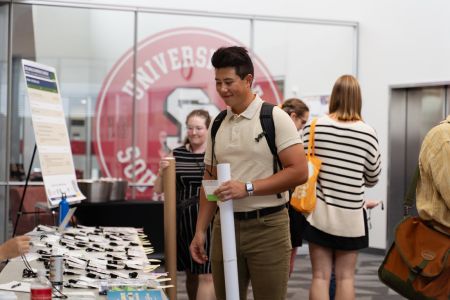A student holds a rolled up poster near a conference registration table.
