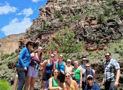 New Mexico immersion students and faculty leaders group in hiking gear alongside a rocky trailhead, with clouds and blue skies behind.