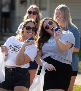 Students hold up small footballs while smiling during the 2025 Homecoming parade.