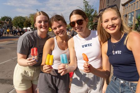 Four Blugolds wearing UWEC attire hold popsicles and smile at the camera.